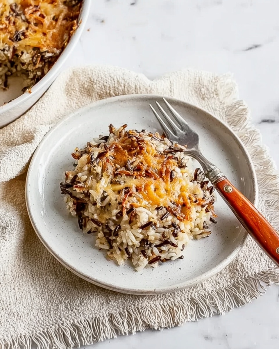 A white plate holds a serving of baked wild rice casserole with a mix of white and dark brown rice grains layered on top of each other, giving a textured look. The rice is topped with light golden melted cheese that mostly covers the rice but lets some grains show through. There is a silver fork with an orange-brown handle resting on the plate’s edge. Next to the plate, there is a cream-colored textured cloth with fringed edges, and part of the casserole dish filled with the same rice and cheese mixture is visible on the left side. The background is a white marbled surface. Photo taken with an iphone --ar 4:5 --v 7