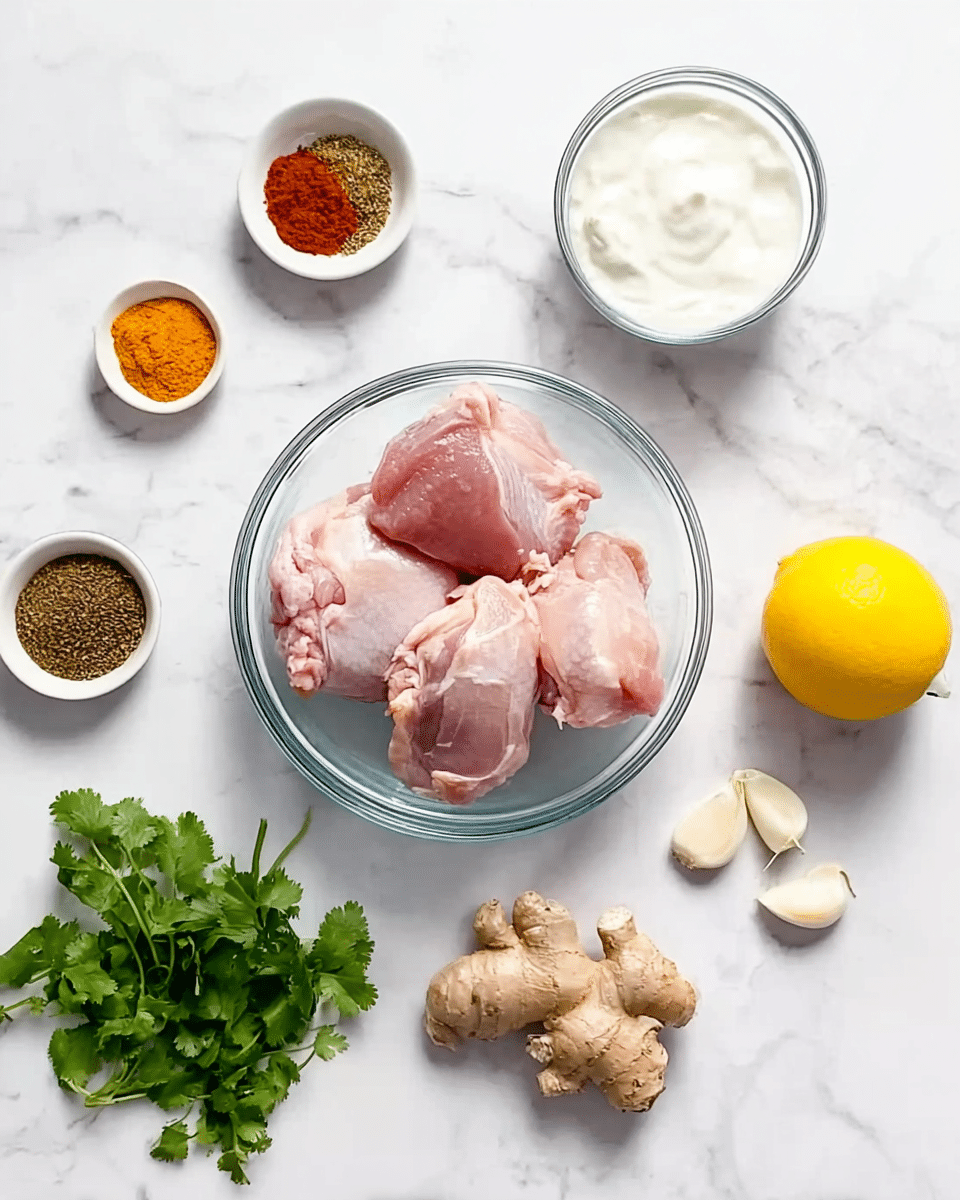 A clear glass bowl with several pieces of raw pink chicken thighs sits in the center on a white marbled surface. To the top right, there is a small clear bowl filled with white yogurt. Below that, a whole yellow lemon is placed. Towards the right top corner, three peeled garlic cloves are laid out near a piece of fresh beige ginger root. On the left side, a small white bowl contains a mix of colorful spices, including brown, orange, and red powders. Below the bowl, a small bunch of fresh green cilantro leaves is arranged. The scene is bright and clear, neatly organized for a cooking prep photo. photo taken with an iphone --ar 4:5 --v 7