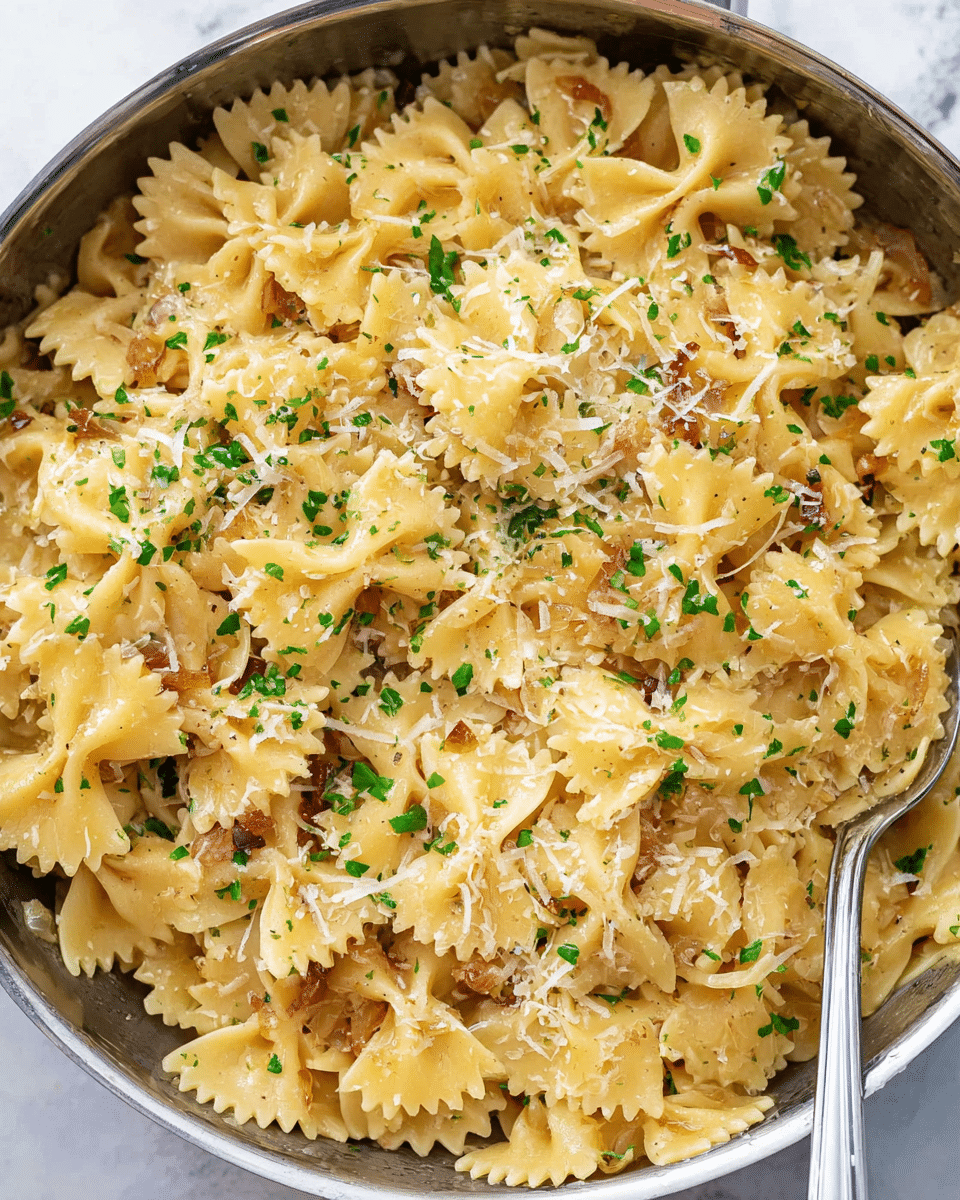 A close-up top view of cooked bow tie pasta in a round metal pan on a white marbled surface, the pasta is light golden yellow with a glossy texture, mixed with bits of caramelized onions visible between the pieces, topped with small sprinkles of finely chopped green herbs and a light dusting of shredded white cheese scattered unevenly across the top. The pan fills the frame fully, and a fork is partially visible on the right side, slightly buried in the pasta, with a very small portion of the white marbled surface visible around the pan edges photo taken with an iphone --ar 4:5 --v 7