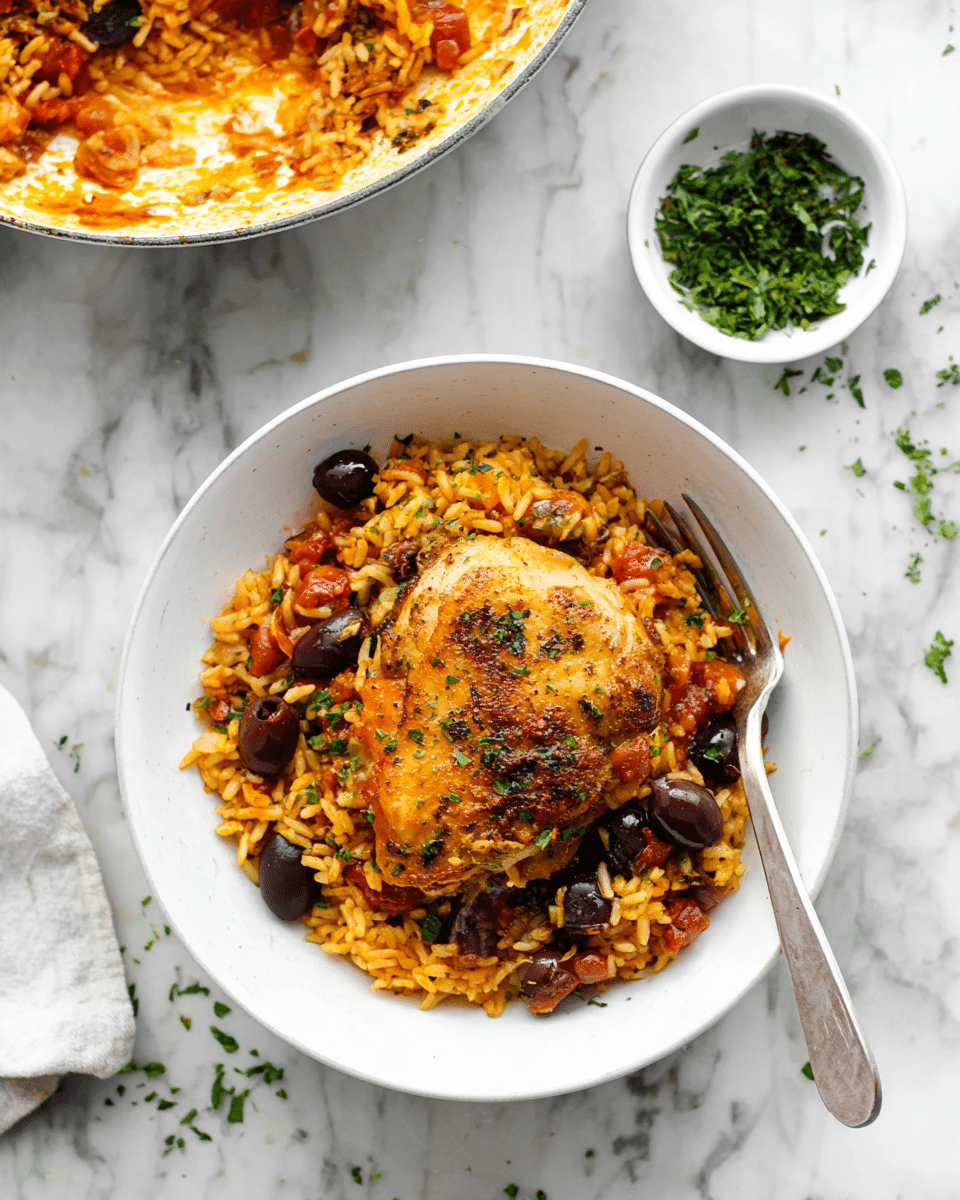 A white bowl sits on a white marbled surface, filled with two main layers: the bottom layer is a bed of orange-yellow rice mixed with dark olives and small green herbs, while the top layer features a golden, crispy piece of cooked chicken seasoned with herbs. A silver fork rests inside the bowl on the right side under the chicken. Nearby, a small white bowl holds chopped green herbs, and in the upper right corner, a white pan contains more of the rice and tomato mix with a silver spoon resting in it. Small scattered green herb pieces decorate the marbled surface around the bowl. Photo taken with an iphone --ar 4:5 --v 7