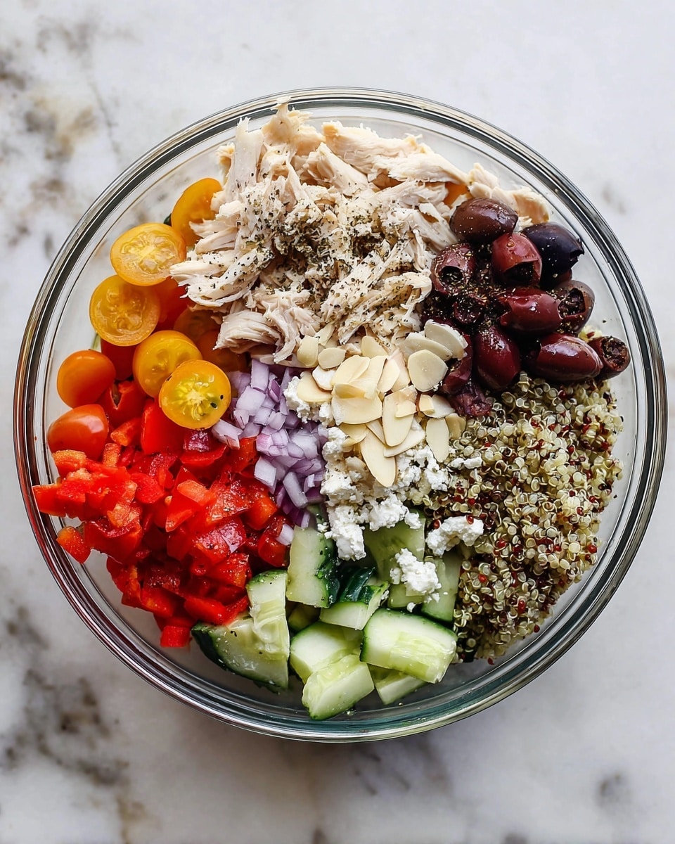 A clear glass bowl sits on a white marbled surface, filled with eight distinct layers of fresh ingredients arranged in a circle. Starting from the top left and moving clockwise, there are shredded light beige chicken pieces sprinkled with black pepper, dark purple sliced olives, bright red and orange halved cherry tomatoes, a mix of white, red, and black quinoa, chunks of light green cucumber with black pepper, red diced roasted red peppers, finely chopped purple onions, and crumbled white cheese with sliced toasted almonds on top. Each ingredient layer is neatly separated and colorful, creating a vibrant and fresh look. Photo taken with an iphone --ar 4:5 --v 7