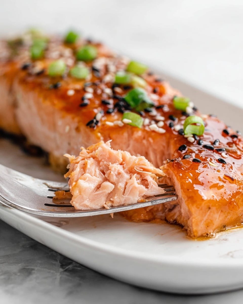 A close-up of a cooked salmon fillet on a white plate with a white marbled texture surface. The salmon has one layer with a bright orange-pink color and a slightly shiny, glazed surface. The top is sprinkled with small black sesame seeds and chopped green onions, adding small dark and bright green spots. The middle part of the salmon is soft and flaky, showing the texture inside with a pale pink tone. A silver fork holds a piece of the salmon, lifting it slightly from the plate. Photo taken with an iphone --ar 4:5 --v 7