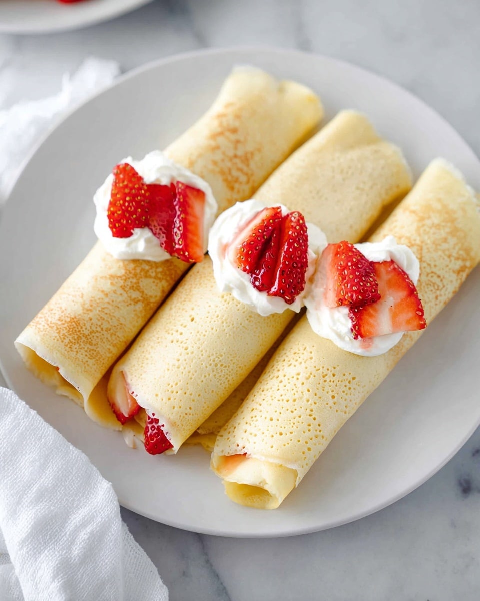 Three light golden crepes are neatly rolled and placed side by side on a white plate, each topped with small dollops of white cream and fresh, bright red strawberry slices arranged close together near the center. The crepes have a smooth, slightly porous texture with edges that gently fold in. The plate rests on a white marbled surface, and a white cloth is partially visible to the left. photo taken with an iphone --ar 4:5 --v 7