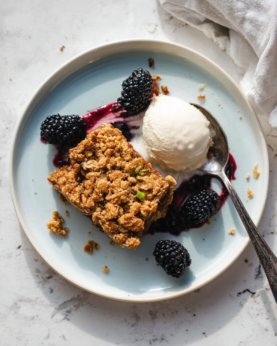 A piece of oatmeal crumble bar sits on a white plate with a light blue inner surface, showing a rough, golden-brown oat topping with a textured look and some small green nut pieces inside. Around the bar, there are a few fresh blackberries with a deep black-purple color and a shiny surface. Next to the bar, there is a scoop of white cream with subtle vanilla specks and a bit of dark berry sauce drizzled over it, creating a subtle purple stain on the cream. A shiny silver spoon lies on the plate under the cream and berries. The plate is placed on a white marbled surface with soft natural lighting. Photo taken with an iphone --ar 4:5 --v 7