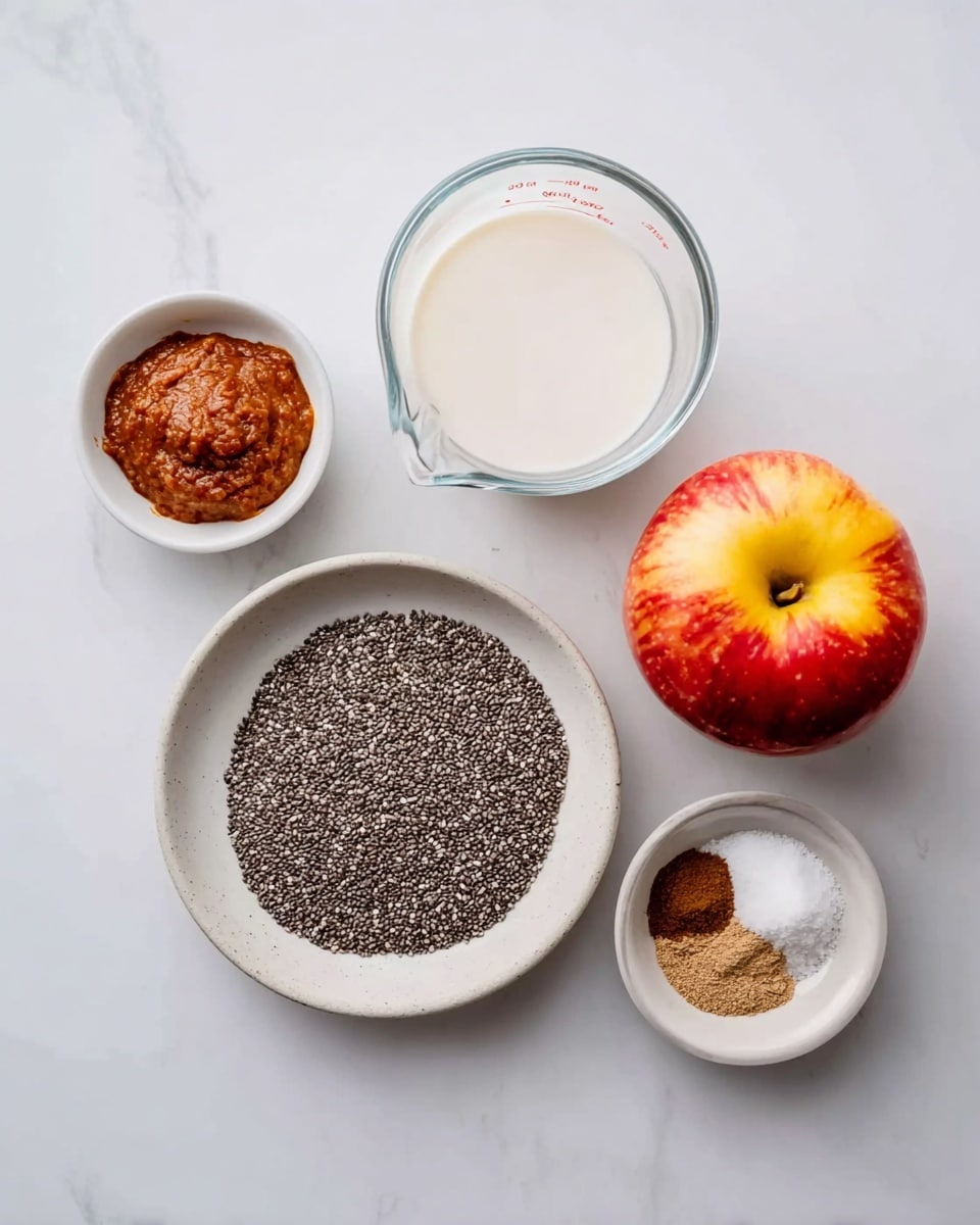 The image shows five white dishes and a clear glass measuring cup on a white marbled surface. In the center, there is a white round plate filled with a single layer of small black and white chia seeds. Above it to the right is a clear glass measuring cup filled with white liquid. To the right of the plate is a whole red and yellow apple with a smooth texture. To the left of the plate are two small white bowls, one filled with a thick, reddish-brown paste and the other with a mix of white granulated ingredients and brown spices in small piles. The arrangement is clean and evenly spaced, with neutral colors and simple textures. Photo taken with an iphone --ar 4:5 --v 7