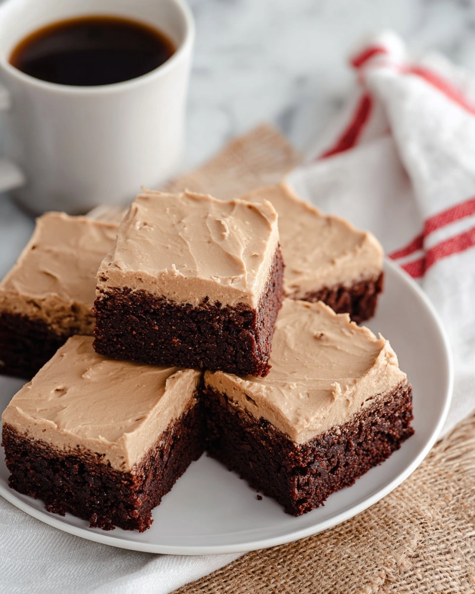 A white plate holds five square brownies neatly stacked, each brownie showing two clear layers: a dark brown, dense bottom layer with a textured surface, and a thick, smooth top layer of light brown frosting with subtle swirls and small cracks. The plate sits on a white marbled surface with a beige burlap fabric partially beneath it and a white napkin with red stripes nearby. A white cup filled with dark coffee is partly visible to the upper left of the plate. photo taken with an iphone --ar 4:5 --v 7