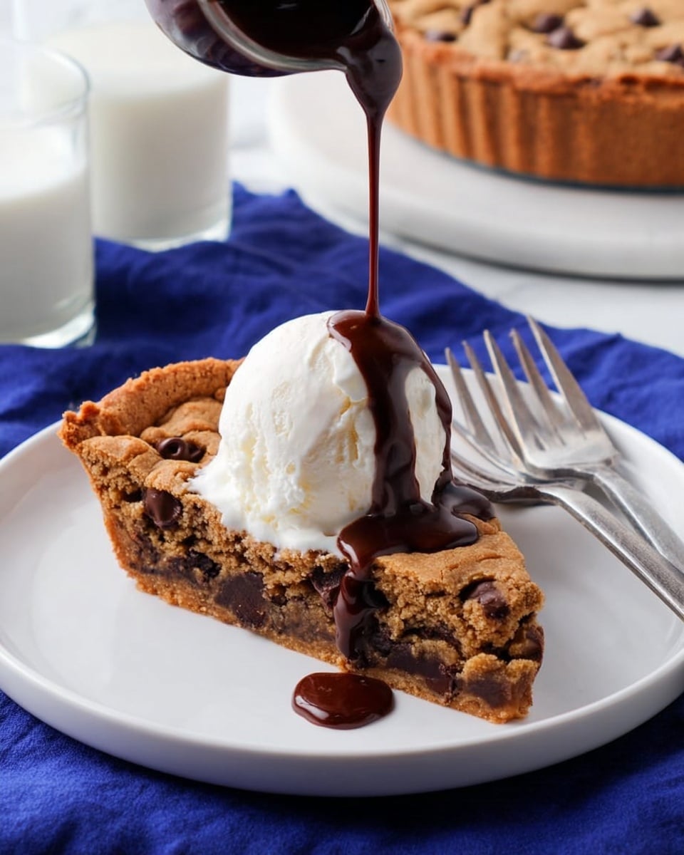 A slice of thick cookie pie on a white plate, with a rough, golden-brown outer crust and a darker, soft chocolate chip center layer visible inside. On top of the slice is a smooth, white scoop of ice cream, and a dark chocolate sauce is being poured over the ice cream from a small dark container, with the sauce creating a shiny, rich coating. The plate sits on a deep blue cloth, and in the background on a white marbled surface, a round cookie pie with chocolate chips is on another white plate, next to two silver forks and a glass of milk. photo taken with an iphone --ar 4:5 --v 7