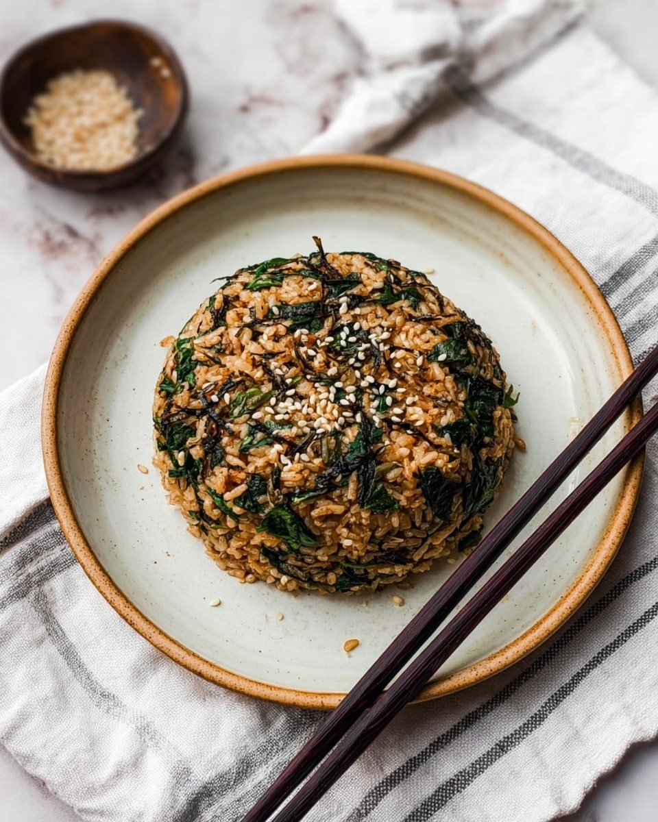 A round mound of fried rice mixed with dark green leafy pieces and small brown bits sits in the center of a white plate with a light brown rim. The rice is sprinkled with white sesame seeds on top. Black chopsticks rest diagonally across the plate’s right side. The plate is placed on a white cloth with thin gray stripes, all set on a white marbled texture surface. Photo taken with an iphone --ar 4:5 --v 7
