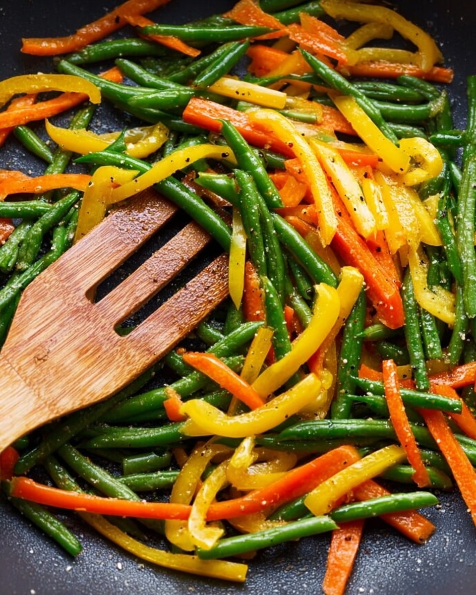 The image shows a close-up of colorful cooked vegetables in a dark pan, with green beans, thin orange carrot sticks, and long yellow pepper strips mixed together. The vegetables are shiny and look soft with a light sprinkle of black pepper. A wooden spatula is placed on the left side, slightly covered by the vegetables. The background is a white marbled texture. photo taken with an iphone --ar 4:5 --v 7