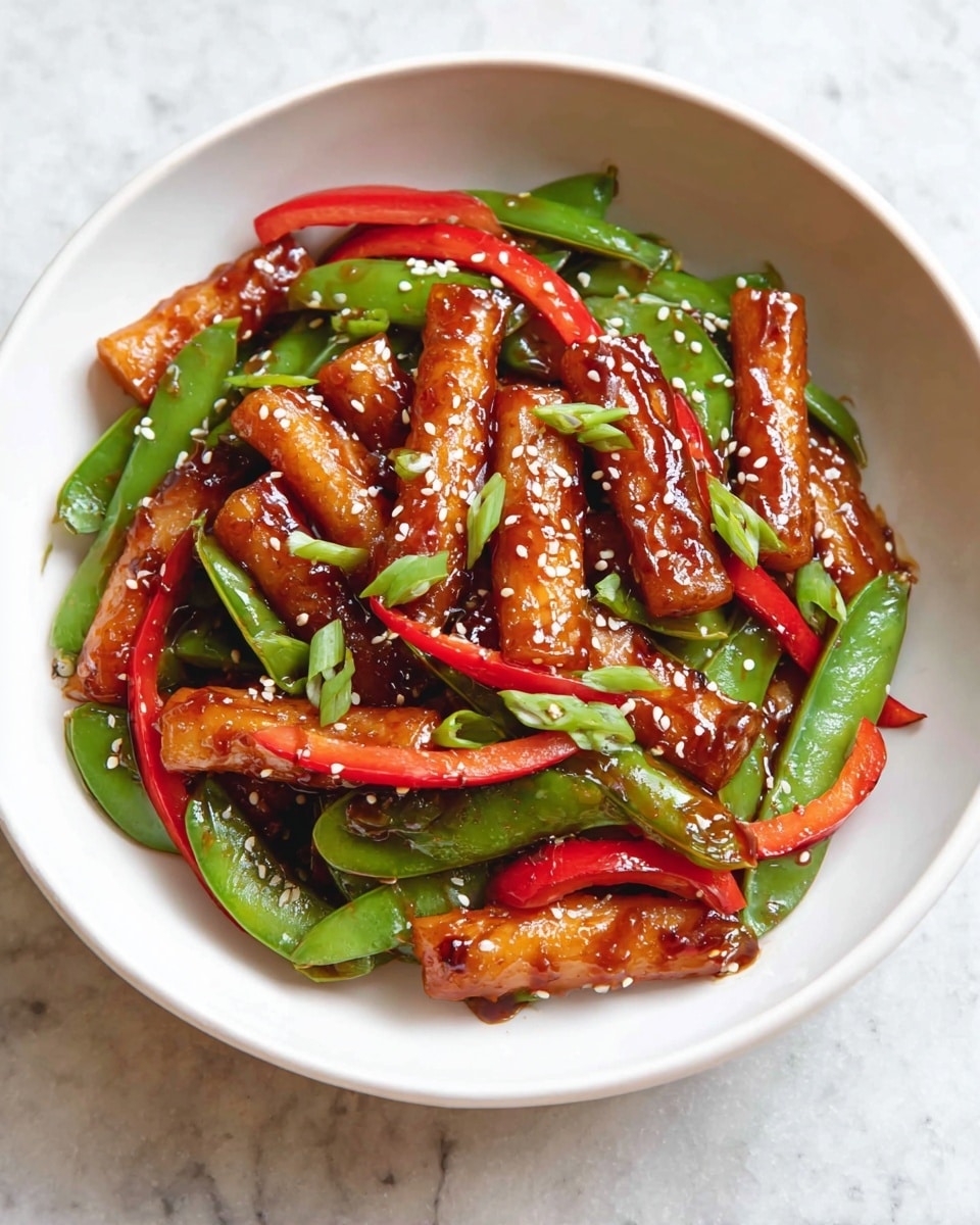 A white bowl filled with a colorful stir-fry dish, showing three main layers: the bottom layer has bright green snap peas and thin red bell pepper strips scattered throughout; the middle layer contains light brown glazed rice cake pieces shaped like short sticks, shiny with sauce and placed evenly across the bowl; the top layer is sprinkled with small white sesame seeds and small green onion slices that add freshness and texture, all presented on a white marbled surface. photo taken with an iphone --ar 4:5 --v 7