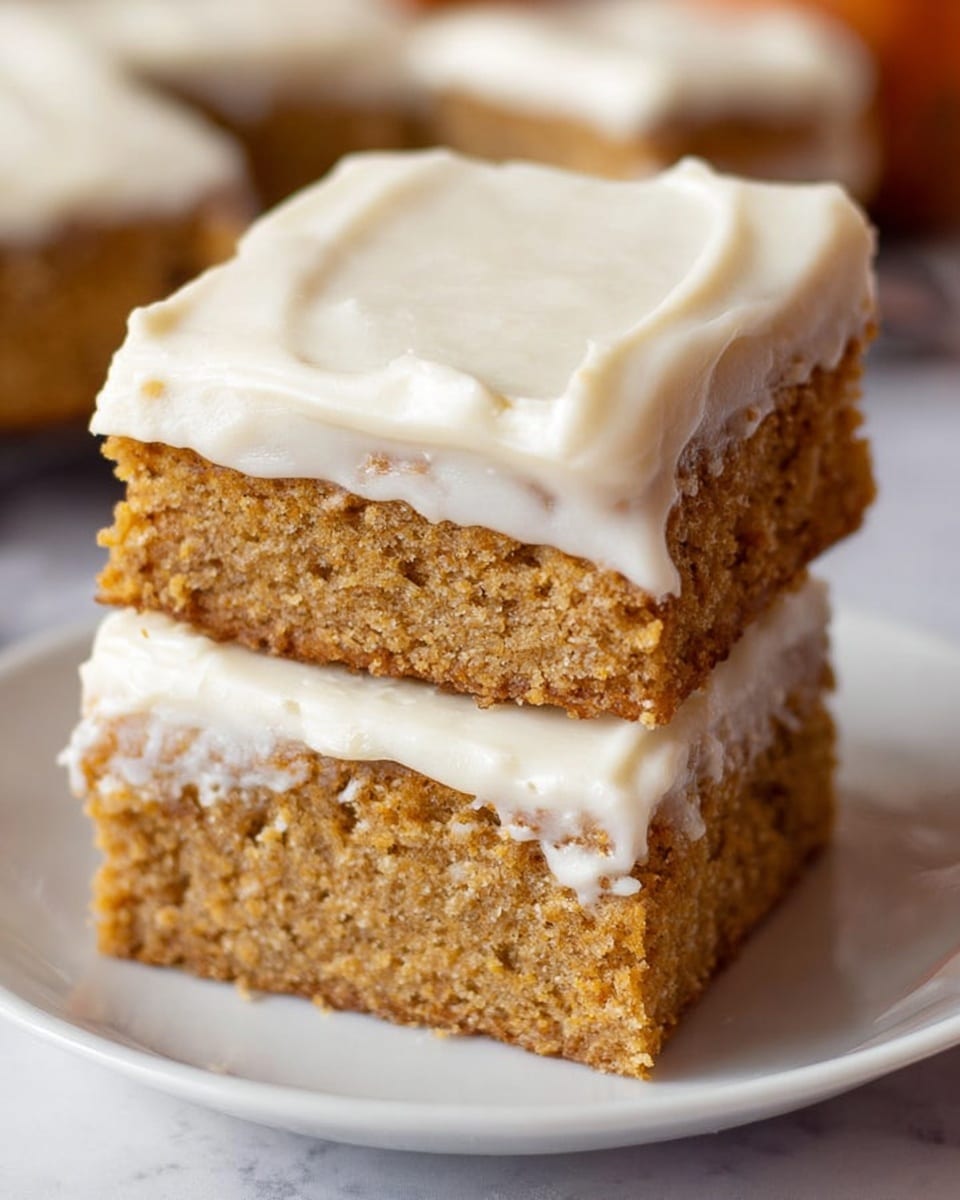 The image shows two square pieces of moist cake stacked on a white plate, each piece having two visible layers. The bottom layer is a thick, soft, light brown cake with a crumbly texture. On top of the cake is a thick, creamy white frosting that covers the whole surface of each piece and spills slightly over the edges. The background is a white marbled surface, and some blurred cake pieces can be seen in the distance. photo taken with an iphone --ar 4:5 --v 7
