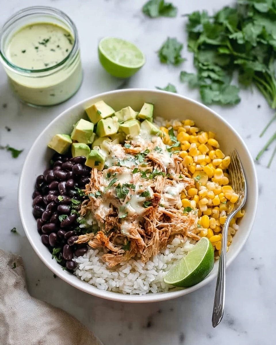 A white bowl sits on a white marbled surface, filled with several colorful layers. At the bottom is a bed of white rice, topped in the center with shredded chicken mixed with light sauce and sprinkled with chopped green herbs. To the left of the chicken are black beans, to the right is bright yellow corn with small green bits mixed in. At the top left side, there are light green cubes of avocado, and on the bottom right edge of the chicken and rice, there is a green lime wedge. A silver fork is resting on the edge of the bowl. In the background, there is a small glass container with a creamy green dressing, some lime wedges, and fresh green herbs scattered around. Photo taken with an iphone --ar 4:5 --v 7