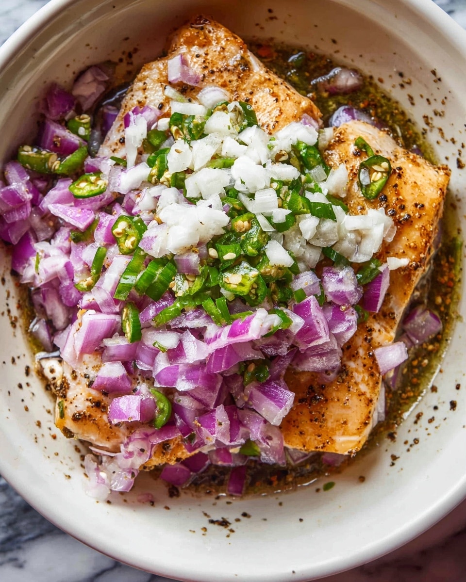 A white bowl contains two pieces of golden-brown cooked fish on the bottom layer, sprinkled with black pepper. On top of the fish, there is a layer of finely chopped red onions with a purple and white color, mixed with small green pieces of fresh chilies. Over the chili and onion, there is a generous layer of finely chopped white garlic. The background is a white marbled texture. Photo taken with an iphone --ar 4:5 --v 7