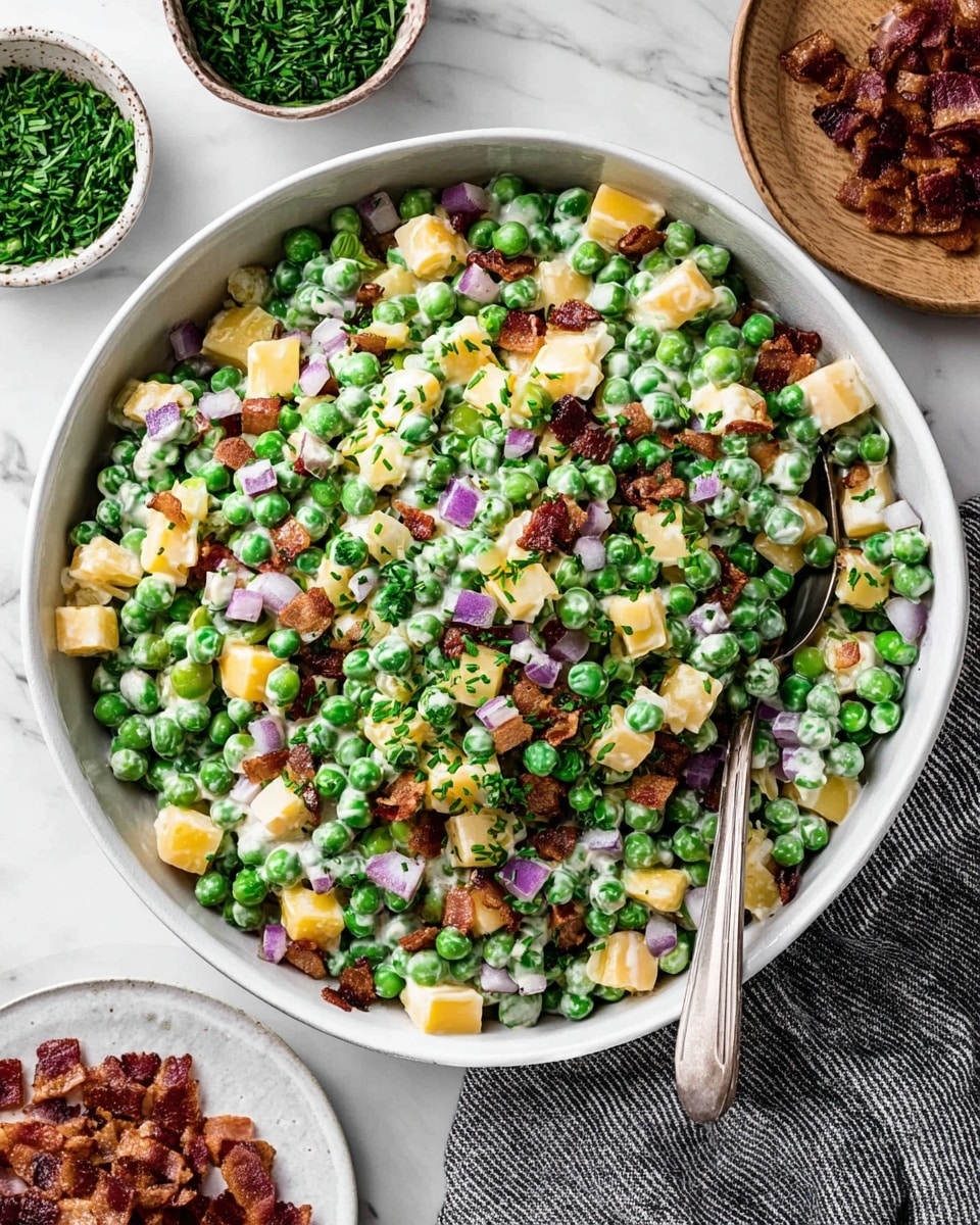 A large white bowl filled with a mix of fresh green peas, small cubes of yellow cheese, and small pieces of crispy bacon. Diced red onion bits add a splash of purple throughout, and the salad is lightly coated with a creamy white dressing. Fresh chopped green herbs are sprinkled on top for color. A metal spoon rests inside the bowl, and the bowl is placed on a white marbled surface. Around the bowl, there are small bowls with chopped herbs and extra bacon pieces on a white plate. A striped dark cloth is partially visible at the bottom right corner. photo taken with an iphone --ar 4:5 --v 7