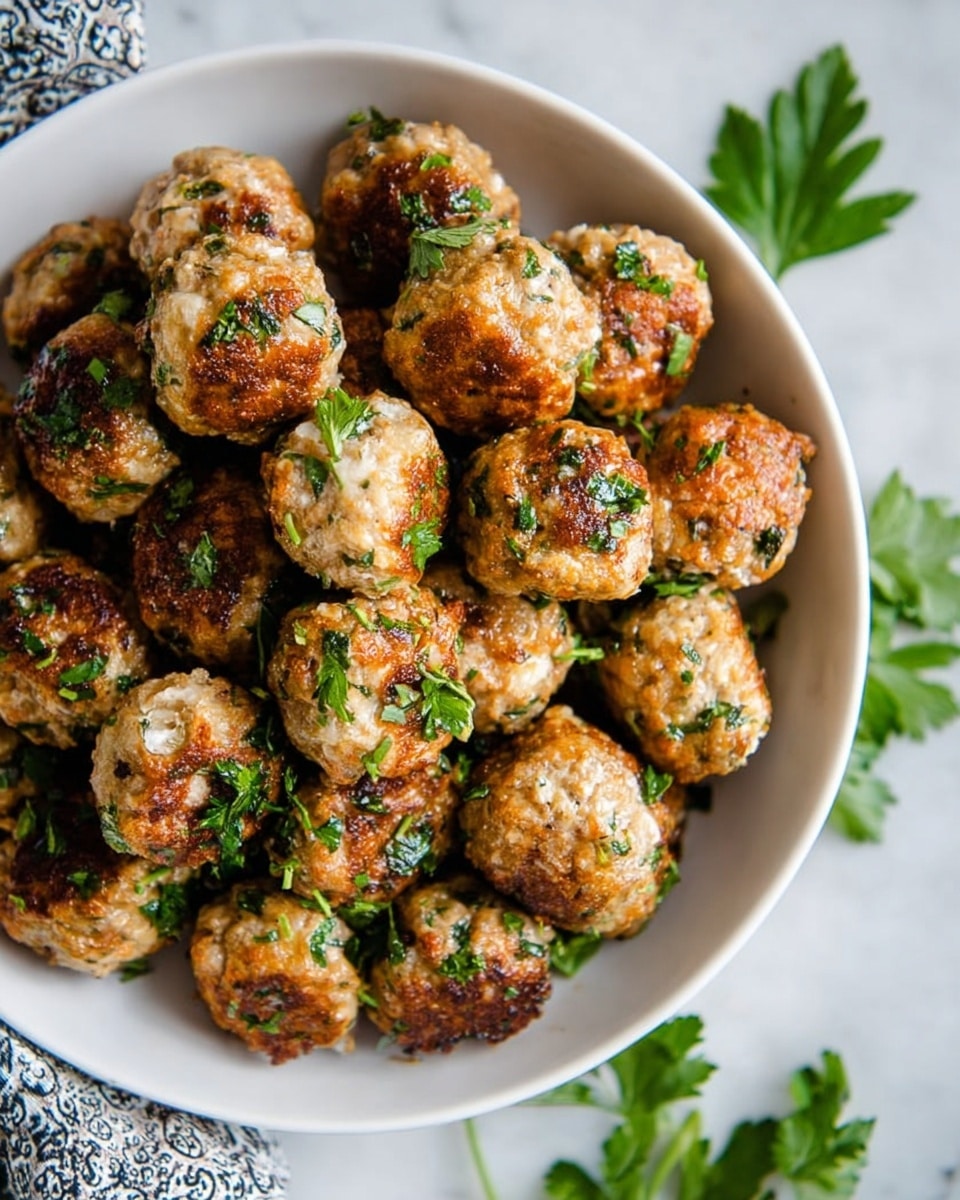 A white bowl filled with many small golden-brown meatballs topped with green chopped parsley, each meatball having a slightly crispy texture on the outside with some white bits inside, sitting on a white marbled surface with some parsley leaves scattered near the bowl and a patterned cloth partially visible on the side, photo taken with an iphone --ar 4:5 --v 7