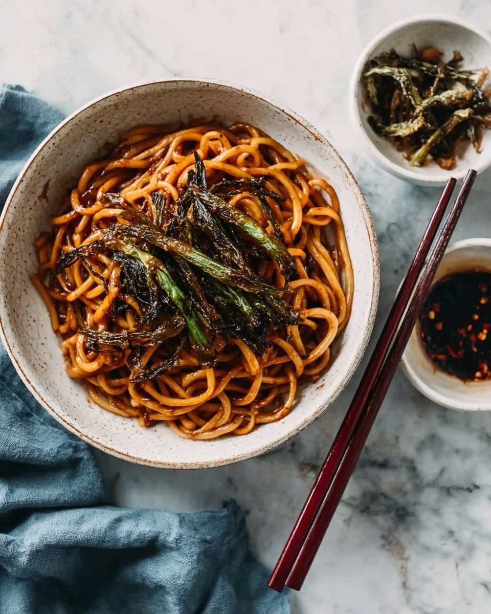 A white speckled bowl filled with a single layer of thick noodles coated in a shiny brown sauce, topped with a small pile of crispy, dark green fried vegetable strips placed in the center. Dark reddish-brown wooden chopsticks rest on the right edge of the bowl, lying parallel. Around the bowl, there are two small white bowls containing similar fried vegetable strips and dark sauce, and a soft blue-gray cloth is casually draped to the left. The whole setting is on a white marbled surface. photo taken with an iphone --ar 4:5 --v 7