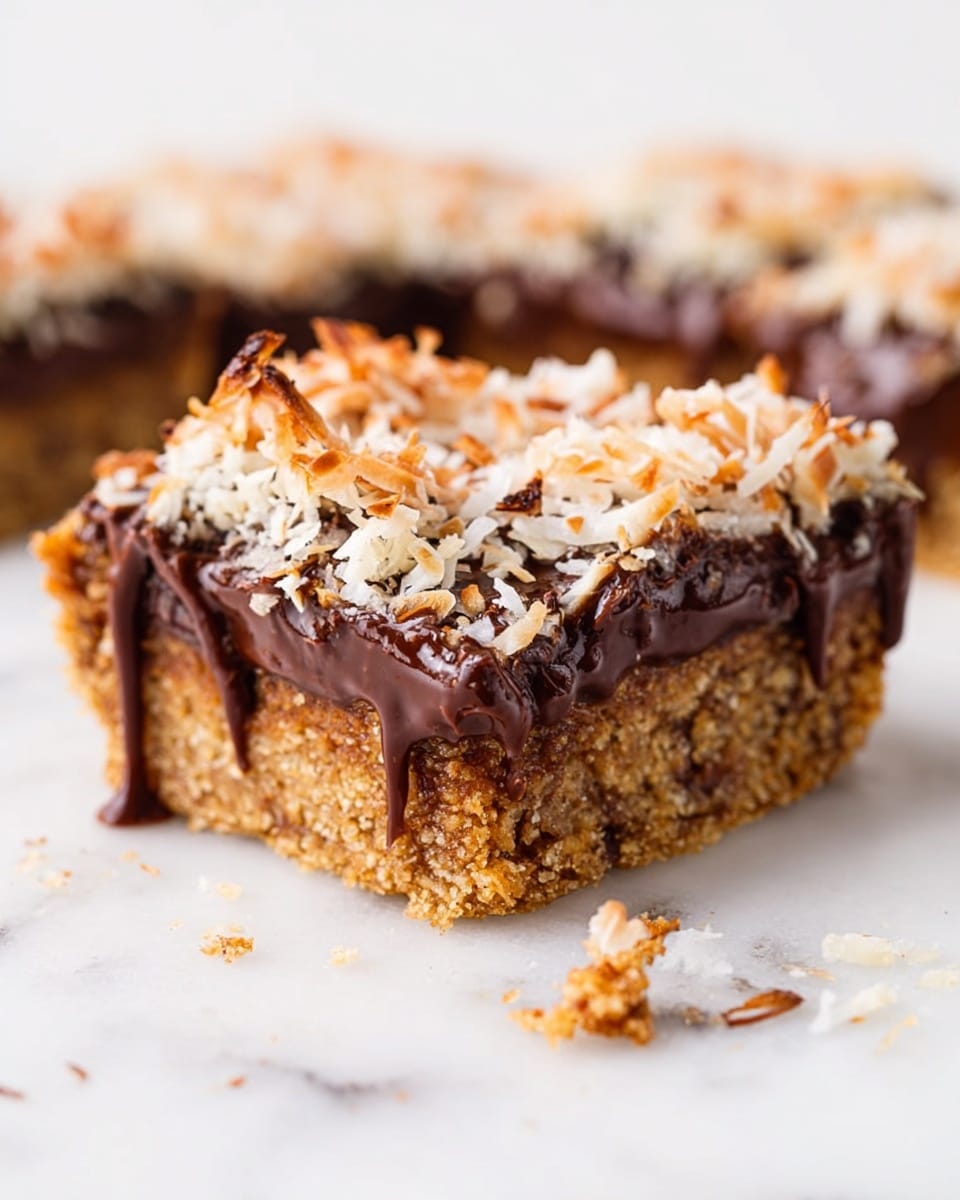 The image shows a close-up of a three-layer bar on a white marbled surface. The bottom layer is a thick, crumbly, golden-brown base. The middle layer is a thick, glossy, dark chocolate spread that looks rich and smooth. The top layer is a rough, textured layer of toasted shredded coconut, which has slight browning and bits scattered around. The chocolate layer drips slightly down the sides, blending into the coconut and base layers. Small crumbs and bits of coconut are scattered on the surface near the bar. Photo taken with an iphone --ar 4:5 --v 7