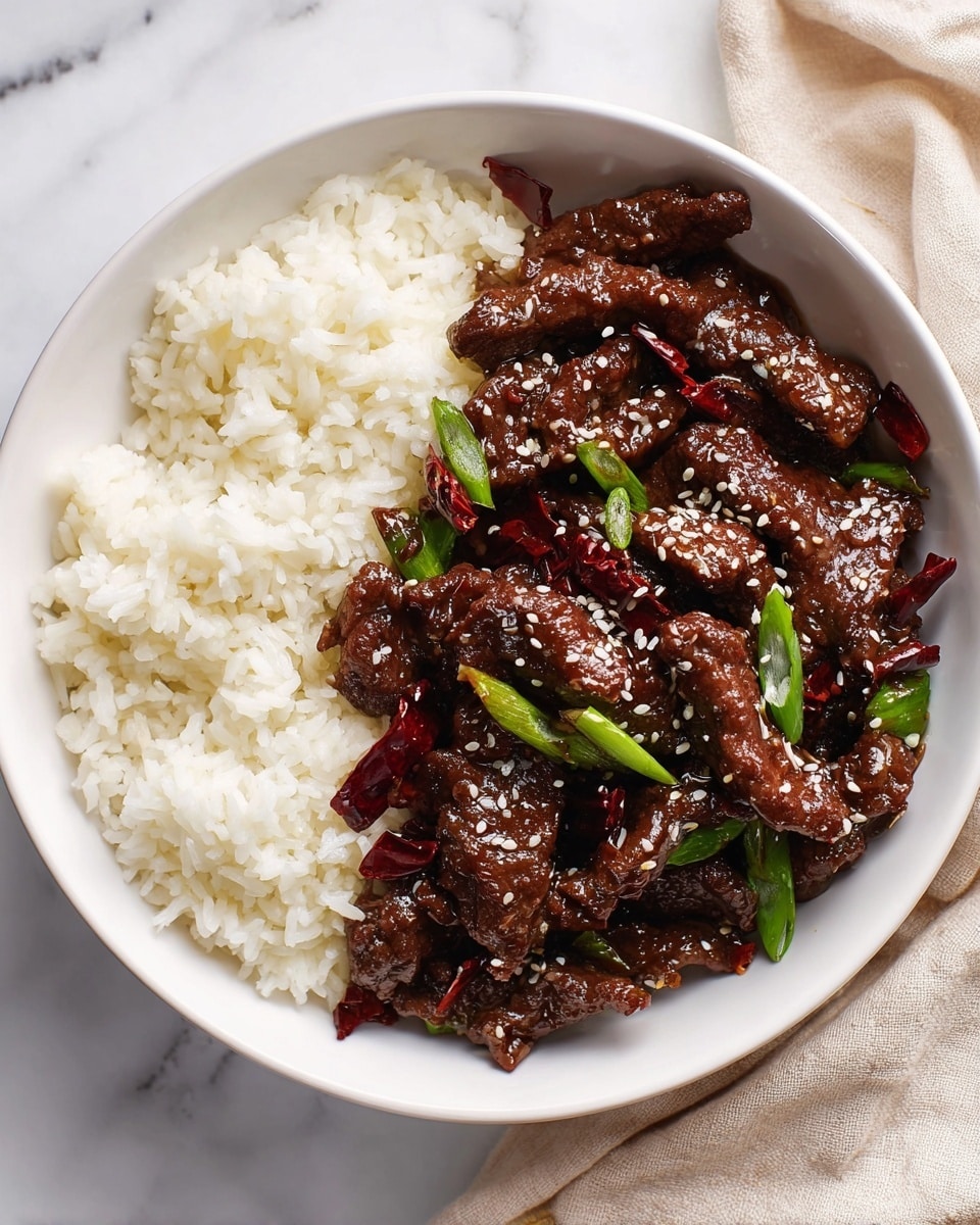 A white round bowl holds two main parts: on the left side, there is a layer of cooked white rice with soft, separated grains; on the right side, there is a thick layer of shiny dark brown beef strips coated in a glossy sauce, mixed with bright green scallion pieces and dark red dried chili pieces; white sesame seeds are sprinkled over the beef for texture. The bowl is set on a white marbled surface with a soft beige cloth partially visible at the top right corner. photo taken with an iphone --ar 4:5 --v 7