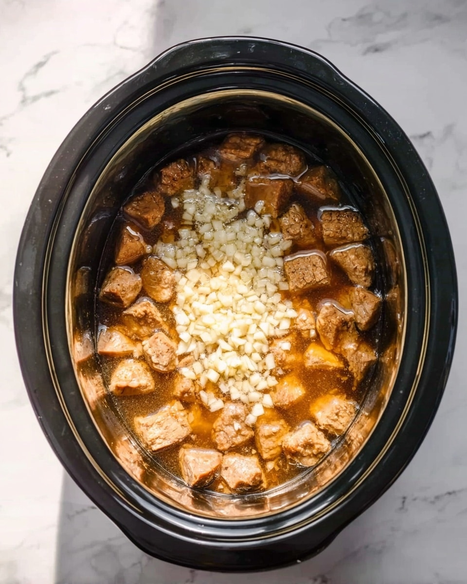 In a black slow cooker, there are three main layers visible. The bottom layer is a shiny, light brown broth filling the cooker halfway. On top of this broth are small, white and slightly translucent chopped pieces of garlic spread mostly in the center. Surrounding the garlic, there are numerous golden-brown chunks of cooked meat with a slightly rough texture, showing seared edges. The slow cooker sits on a white marbled surface with bright lighting casting soft shadows. Photo taken with an iphone --ar 4:5 --v 7