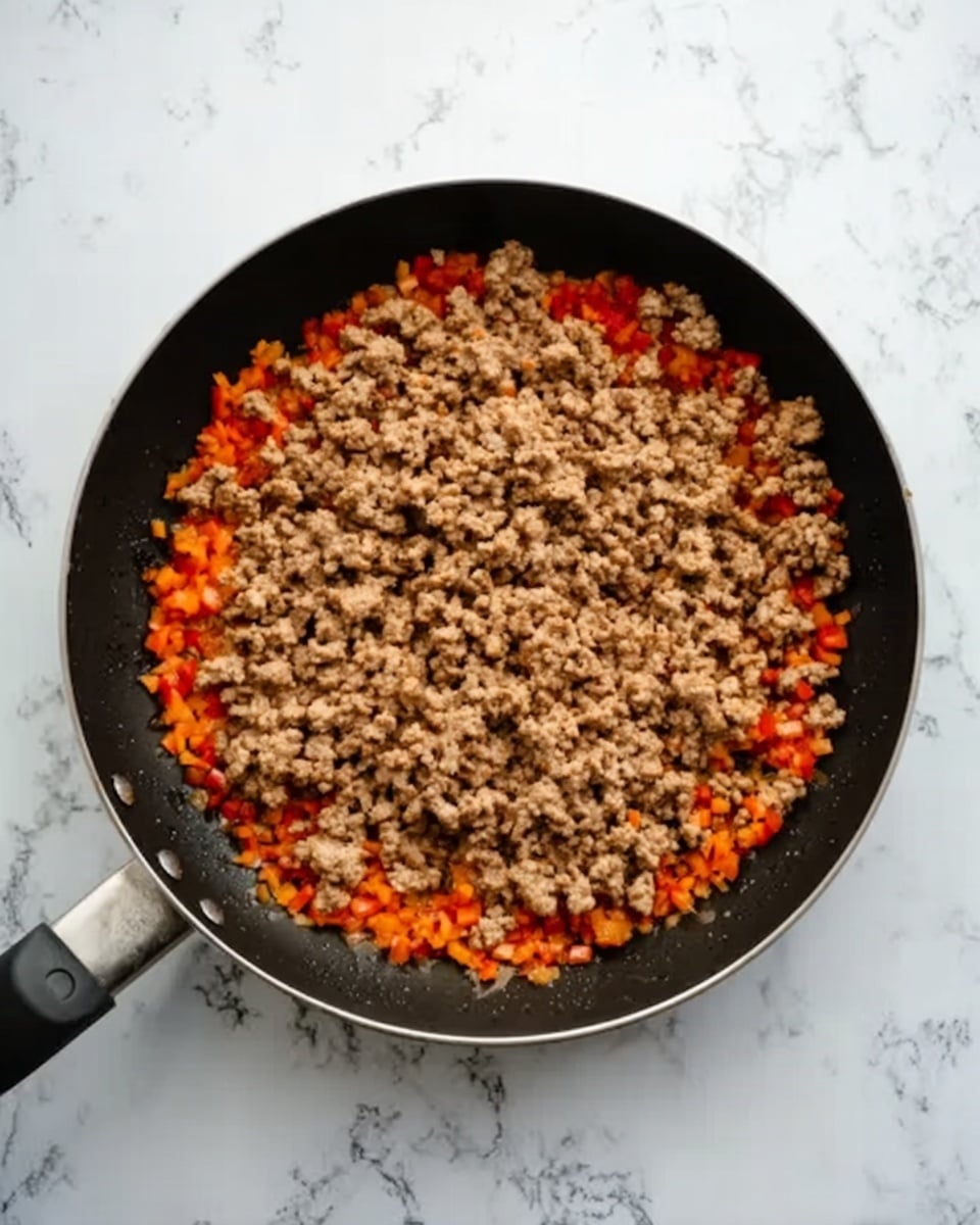 A black frying pan is shown from above on a white marbled surface, filled with one main layer of cooked ground meat in a light brown color, covering most of the pan. Around the edges of the meat, there is a ring of finely chopped orange and red vegetables creating a contrast between the center and the border. The texture of the meat looks crumbly and soft, while the vegetables are small and slightly glossy. Photo taken with an iphone --ar 4:5 --v 7