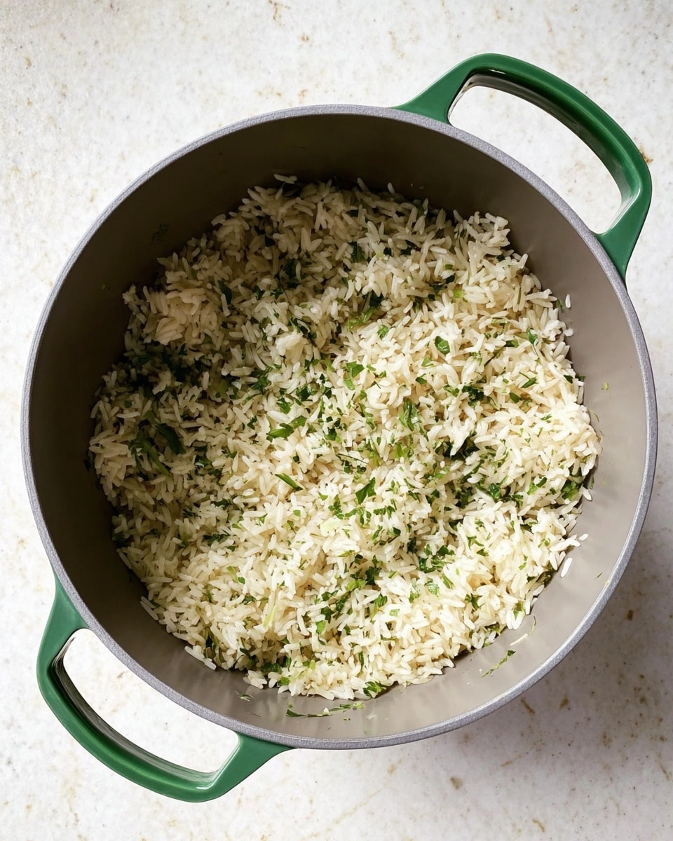 A top view of a single-layer dish of cooked rice mixed with small bits of green herbs in a gray pot with green handles, placed on a white marbled surface. The rice grains are fluffy with slightly browned spots and scattered green herbs for texture and color contrast, filling most of the pot evenly with no other ingredients visible photo taken with an iphone --ar 4:5 --v 7