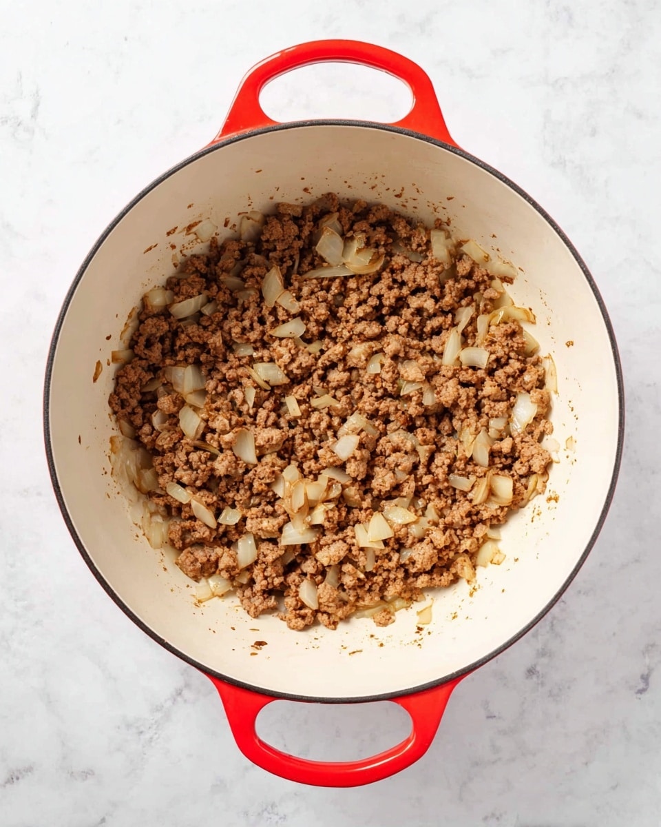 A large white pot with bright red handles is shown from above on a white marbled surface. Inside the pot is one layer of cooked ground meat mixed with diced onions. The meat is brown and crumbly, while the onions are translucent and slightly soft. The mixture is evenly spread across the center of the pot, with some small bits scattered around. photo taken with an iphone --ar 4:5 --v 7