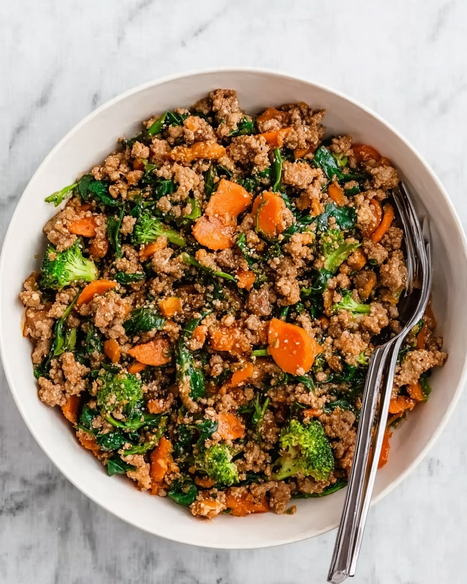 A white bowl filled with a mix of cooked ground meat, bright green broccoli florets, chopped orange carrots, and dark green spinach leaves. The ingredients are evenly spread together, with a slightly crumbly texture from the meat and vibrant colors from the vegetables. Two silver forks rest on the right side inside the bowl, partially covered by the food. The bowl sits on a white marbled surface. photo taken with an iphone --ar 4:5 --v 7
