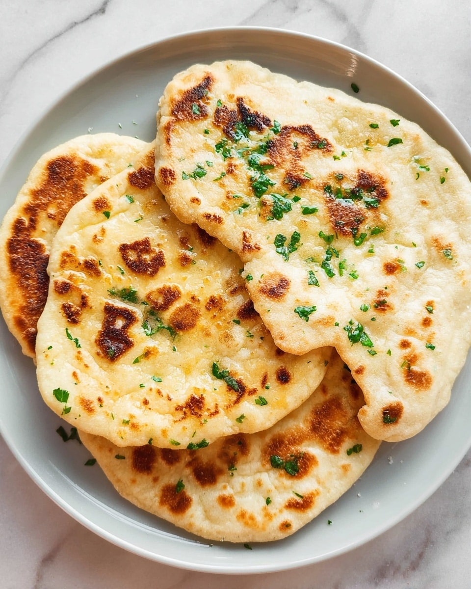 The image shows three pieces of flatbread stacked on a white plate. The bottom two layers are round and golden brown with some darker brown spots, while the top flatbread is more irregular in shape, lighter in color with toasted spots and a bubbly texture. Each flatbread is sprinkled with small, bright green herb pieces that give a fresh look. The plate rests on a white marbled surface. Photo taken with an iphone --ar 4:5 --v 7