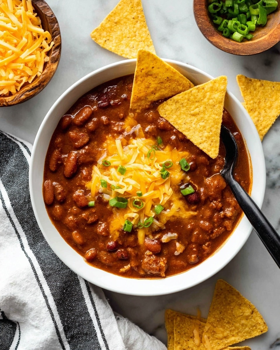 A white bowl filled with thick brown chili made of beans and meat pieces, topped with melted yellow cheese and chopped green onions in the center. Two triangular yellow tortilla chips are placed inside the bowl, leaning on one side. A black spoon is partly inside the chili on the right side. Around the bowl, more yellow tortilla chips are scattered on a white marbled surface. Two wooden bowls, one filled with shredded yellow cheddar cheese and the other with chopped green onions, are partially visible at the top right corner. A white cloth with black stripes is at the bottom left corner. Photo taken with an iphone --ar 4:5 --v 7