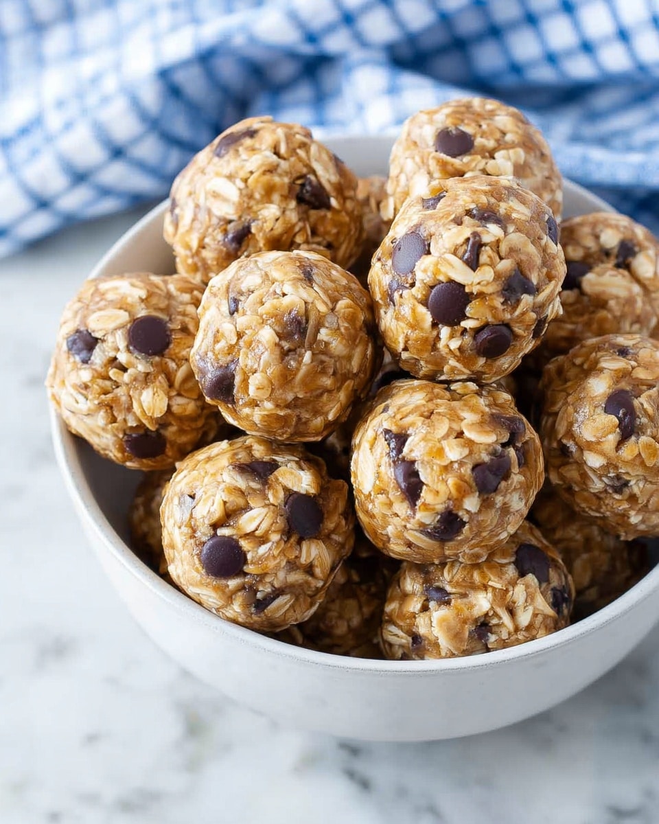 A white bowl filled with small round oatmeal balls mixed with dark chocolate chips, showing a rough textured surface made of oats and chocolate chips evenly spread. The balls are stacked closely together, filling the bowl fully, with some oats and chocolate chips visible on their light brown surface. The bowl sits on a white marbled surface, and a blue and white checkered cloth is slightly visible on the upper right side. Photo taken with an iphone --ar 4:5 --v 7