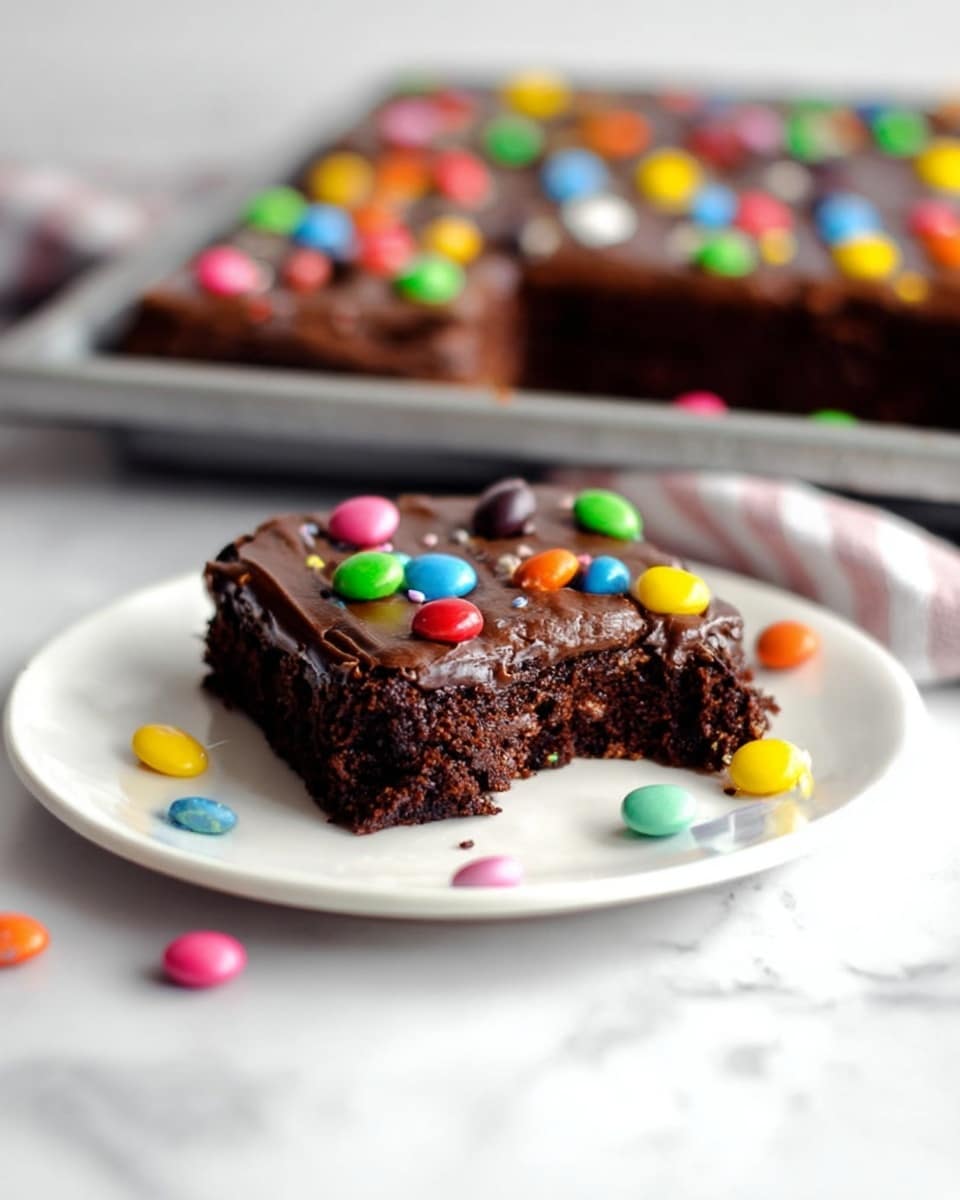 The image shows a single rectangular chocolate brownie on a white plate with a bite taken out of the corner, revealing its moist and rich dark brown inside. The brownie has a smooth, shiny layer of dark chocolate frosting on top, decorated with colorful candy drops in bright red, yellow, green, blue, pink, orange, and purple scattered over the surface and some fallen beside the brownie. In the background, there is a larger tray with more brownies, also topped with the same colorful candy drops and frosting, all placed on a white marbled surface. photo taken with an iphone --ar 4:5 --v 7