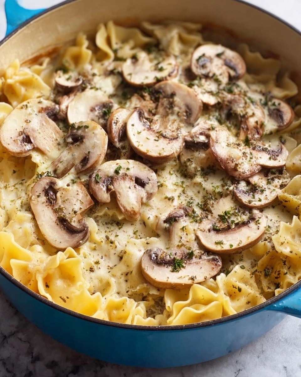 A blue pot filled with three visible layers: at the bottom is a white marbled textured surface beneath the pot, above it is a layer of pale yellow pasta with wide ruffled edges, over this is a creamy light yellow sauce covering the pasta, and the top layer consists of sliced fresh white mushrooms with light brown gills and specks of dried green herbs scattered over the mushrooms and sauce. photo taken with an iphone --ar 4:5 --v 7
