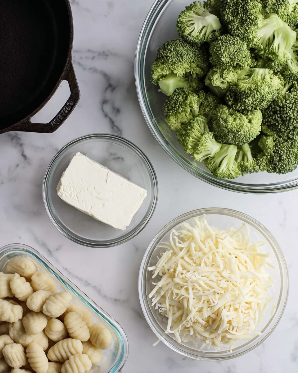 The image shows a clear glass bowl filled with bright green broccoli florets on the right side of a white marbled surface. Below the bowl is another clear glass bowl filled with shredded white cheese. Below that and closer to the center is a small clear glass bowl with a block of white cream cheese inside. To the left is a clear plastic container of uncooked gnocchi with a light beige color, placed near the bottom left corner. Part of a black cast iron pan with a handle is seen on the top left on the white marbled surface. photo taken with an iphone --ar 4:5 --v 7