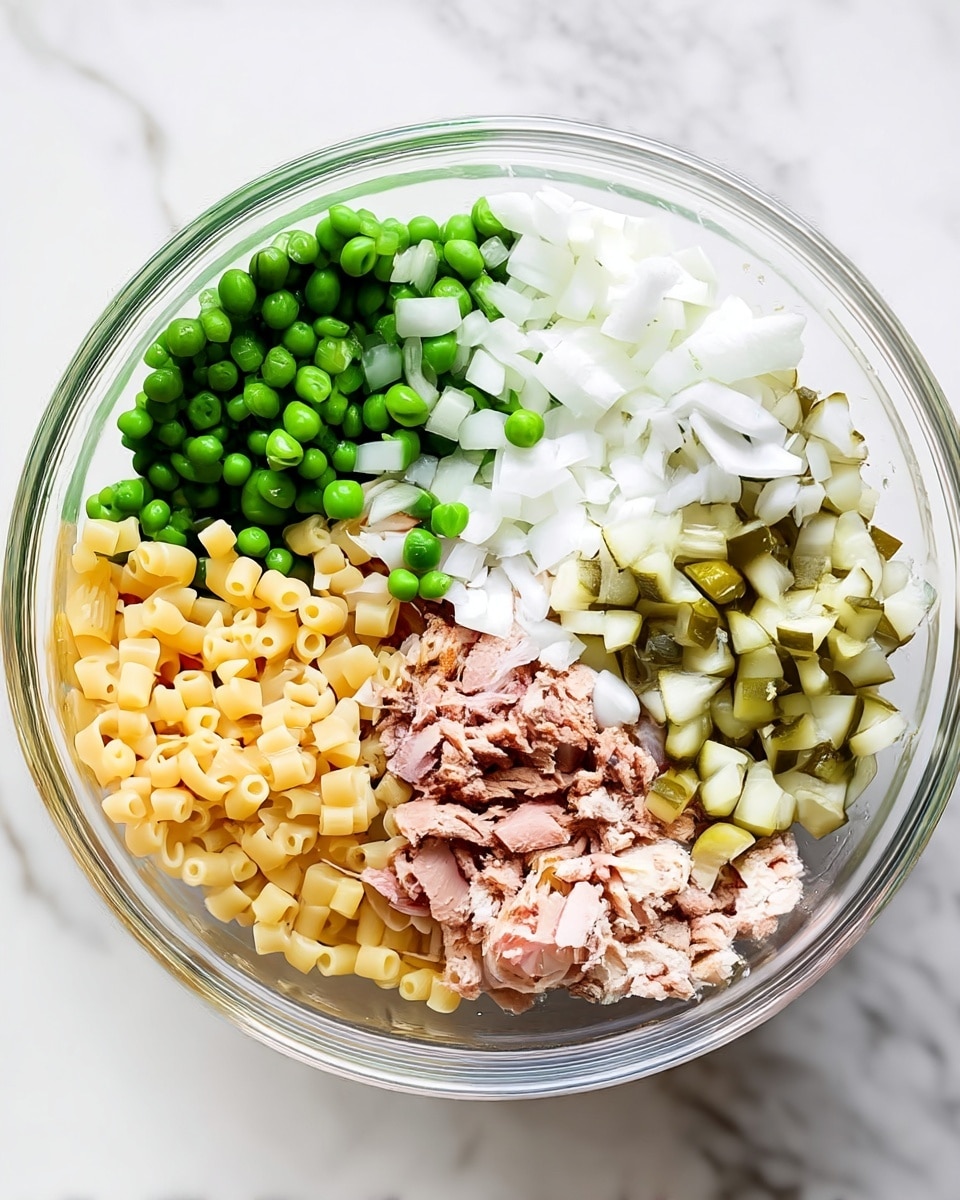 A clear glass bowl holds five separate layers of salad ingredients, each taking up about one-fifth of the bowl. Starting from the top left, there is a layer of bright green peas, next to it on the right a layer of white diced onions, then below that a layer of diced pickles in a mix of light green and beige. Below the onions and pickles is a layer of light pink shredded tuna. Finally, at the bottom left of the bowl is a layer of small, pale yellow pasta tubes. The bowl sits on a white marbled surface. photo taken with an iphone --ar 4:5 --v 7