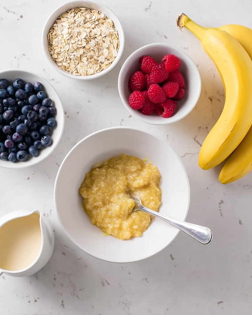 A white bowl in the center holds a yellow mashed banana being mixed with a silver fork. Around this bowl are four small white bowls: one filled with plain oats at the top center, one with bright red raspberries on the top right, and one with dark blue blueberries on the left side. A small white pitcher with a cream-colored liquid is just below the blueberry bowl. Three yellow bananas are placed on the white marbled surface to the right of the main bowl. The scene is lit softly and arranged neatly on a white marbled texture. photo taken with an iphone --ar 4:5 --v 7