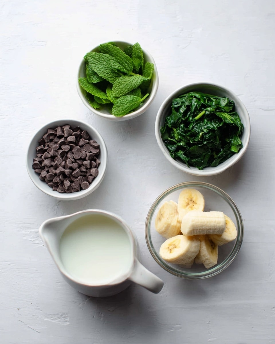 The image shows five small white bowls and one white jug on a white marbled surface. One bowl has fresh green mint leaves, another holds dark green chopped spinach, and a third is filled with small dark brown chocolate chips. A clear glass bowl contains four pieces of peeled banana. The white jug is filled with milk. All items are neatly placed, creating a clean and simple arrangement. photo taken with an iphone --ar 4:5 --v 7