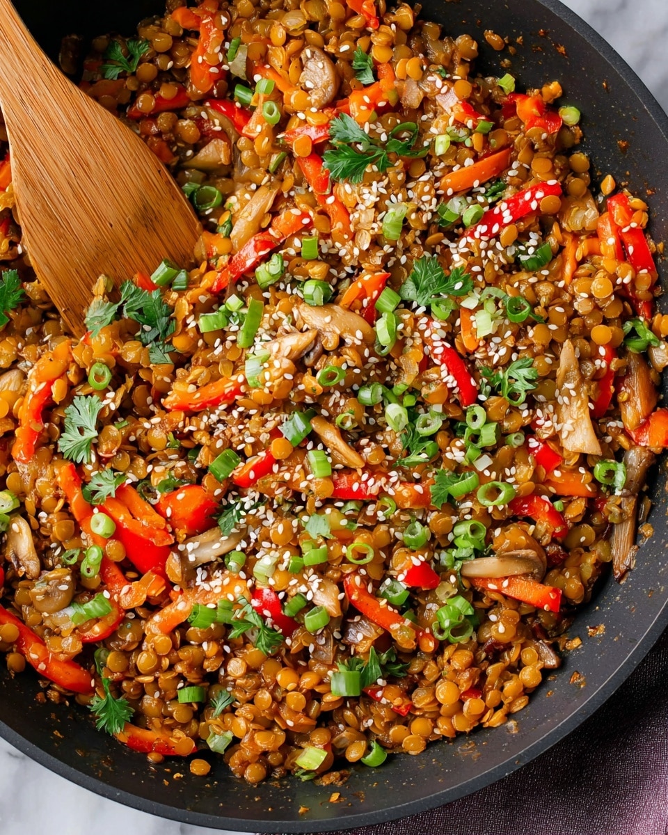 The image shows a close-up of a black pan filled with a colorful stir-fry dish made of orange lentils mixed with small bright orange carrot strips, diced red bell peppers, and light beige mushroom pieces. The dish is topped with scattered white sesame seeds and fresh green onion slices along with green cilantro leaves, adding a fresh touch of color. A wooden spatula rests on the left side, partly mixed into the food, all placed on a white marbled surface. Photo taken with an iphone --ar 4:5 --v 7