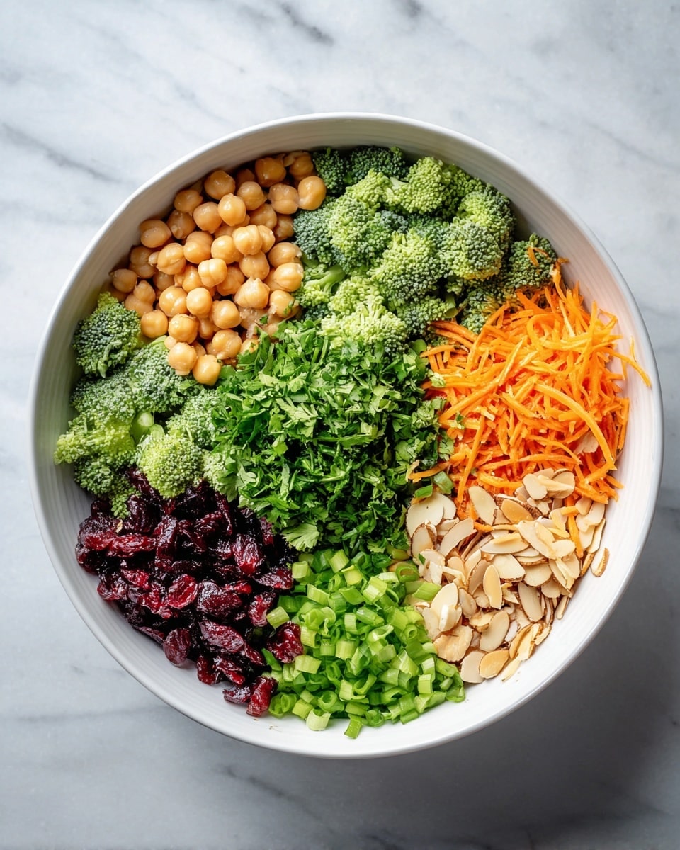 A white bowl sits on a white marbled surface filled with six distinct layers of ingredients arranged side by side. Starting from the top left, there are light brown chickpeas, next to them are fresh dark green broccoli florets. In the middle is a large pile of finely chopped bright green cilantro. To the right of the cilantro are thinly sliced light brown almonds. Below the almonds is a pile of orange shredded carrots, and left of the carrots is a layer of chopped green onions. At the bottom left next to the chickpeas are deep red dried cranberries. Each ingredient is clearly separated, showing different colors and textures, all arranged in a neat, circular pattern. Photo taken with an iphone --ar 4:5 --v 7