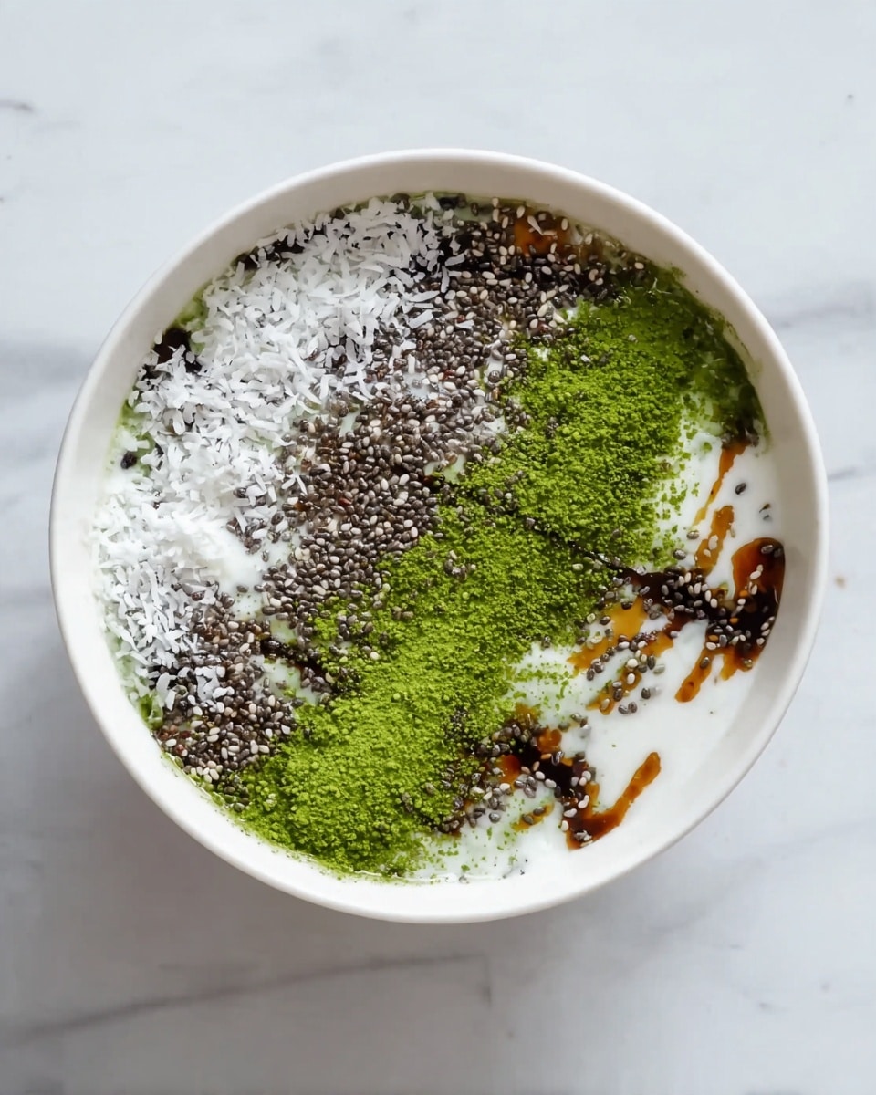 A white bowl on a white marbled surface contains a dish with multiple layers. The bottom layer is white and smooth, likely cream or yogurt. On top, there are scattered small black chia seeds mostly on the lower half, with white shredded coconut spread on the upper left and right sides. Bright green matcha powder is sprinkled in thick lines across the top center and right side. Dark brown syrup is drizzled diagonally from top right to bottom left, creating a contrast with the other colors. The textures mix powdery green, crunchy seeds, and flaky white coconut, all inside the white bowl. Photo taken with an iphone --ar 4:5 --v 7