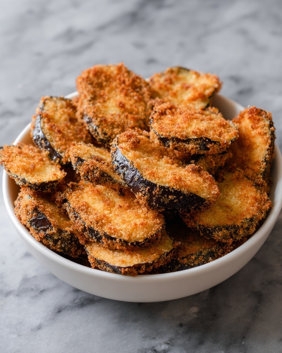 A bowl is filled with many golden brown fried slices of eggplant, each piece showing a crispy, crumb-covered outer layer with a rough texture. The eggplant pieces are stacked closely, some showing the darker purple skin peeking through under the crunchy coating. The bowl itself is white and placed on a white marbled surface, giving a clean, bright look to the setting. photo taken with an iphone --ar 4:5 --v 7