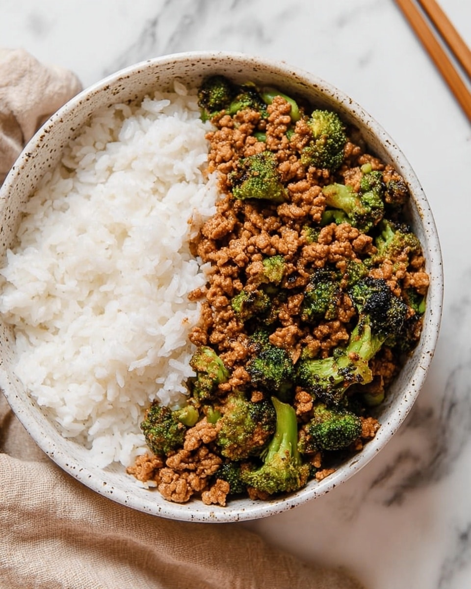 A white speckled bowl filled with two main layers side by side: on the left, a smooth and fluffy white rice layer with visible individual grains, and on the right, a cooked mixture of small minces of meat and bright green broccoli florets, coated in a glossy brown sauce giving a slightly shiny and textured appearance. The bowl sits on a white marbled surface with a beige cloth and chopsticks partially visible at the top right. photo taken with an iphone --ar 4:5 --v 7