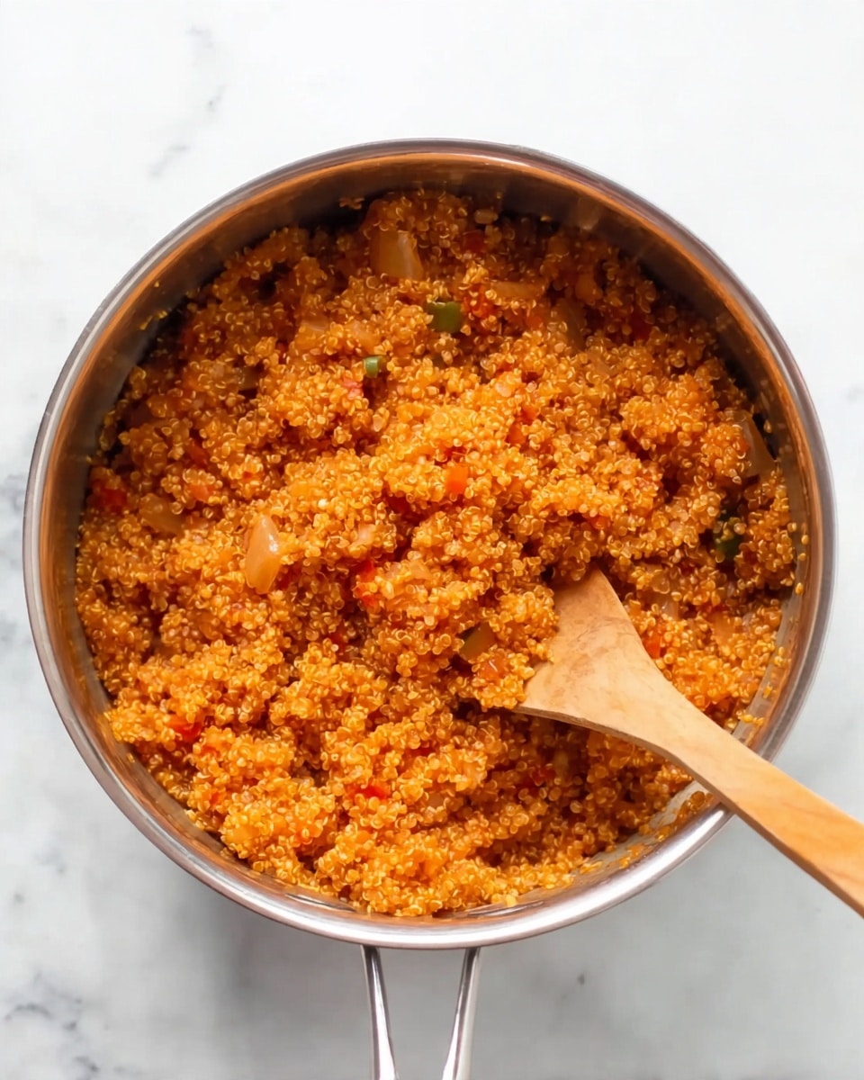 A shiny silver pot is filled with cooked quinoa that is orange in color, with visible small pieces of vegetables like onions and peppers mixed in. A wooden spoon with a long handle is partly buried in the quinoa on the right side of the pot. The pot is placed on a bright white marbled surface. photo taken with an iphone --ar 4:5 --v 7