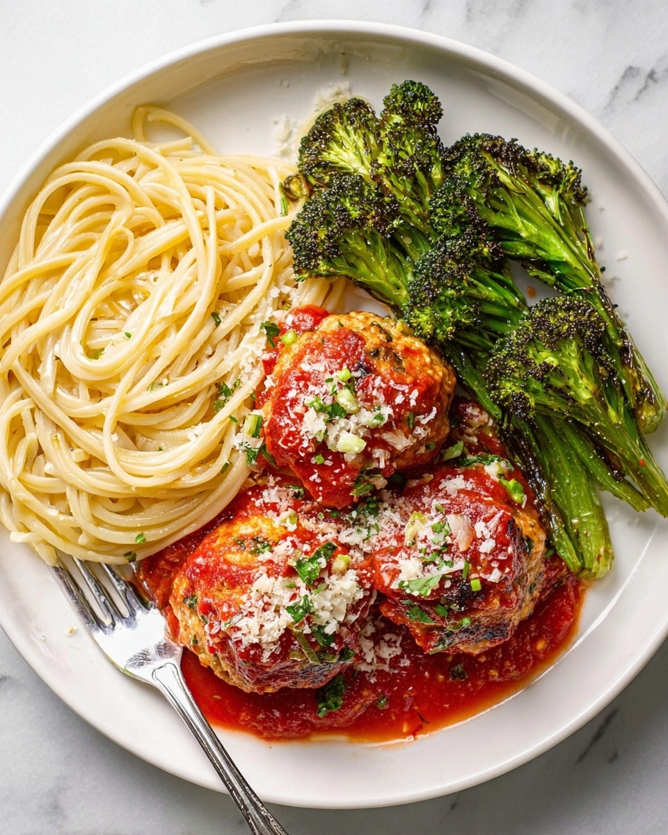 A white plate holds a serving of spaghetti on the left side, with long, thin, pale yellow strands neatly piled. On the right side of the plate, there are three large round meatballs, each covered with red tomato sauce and sprinkled with finely grated white cheese and small bits of green herbs. Above the meatballs, there is a group of bright green broccoli florets with charred edges, adding texture and color contrast. A silver fork is placed in the tomato sauce next to the meatballs on the right edge of the plate. The background is a white marbled texture. photo taken with an iphone --ar 4:5 --v 7