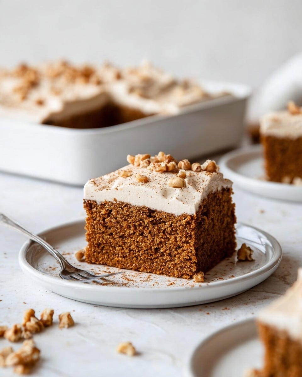 A tall square piece of soft brown cake sits on a white plate with scattered walnut pieces and crumbs around it. The cake has two layers: a thick, moist-looking brown base and a smooth, light cream-colored frosting on top, sprinkled with small walnut pieces and a dusting of cinnamon or spice. In the background, there is a white baking dish holding more of the same cake, placed on a white marbled surface. A silver fork rests next to the cake on the plate. The setting is bright with soft natural light, giving the cake a fresh and inviting appearance photo taken with an iphone --ar 4:5 --v 7