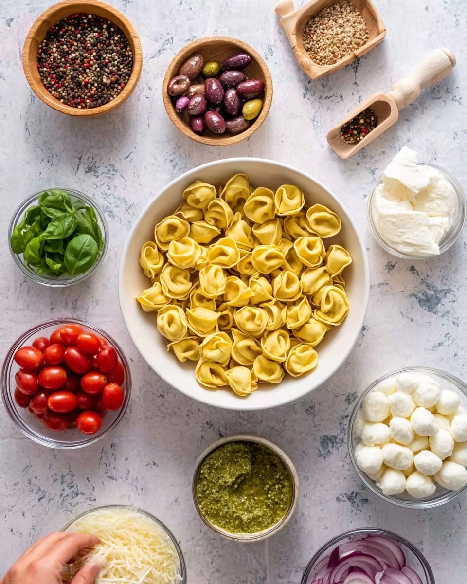 The image shows a white bowl filled with many yellow tortellini pasta pieces, each having a smooth, slightly shiny surface and a round, flower-like shape arranged neatly inside. Surrounding this main bowl are smaller white bowls and glass cups placed on a white marbled surface. Moving clockwise from the tortellini, there is a wooden bowl full of mixed peppercorns with a small wooden scoop, followed by another wooden bowl containing coarse salt and a wooden scoop. Below these, there is a small white bowl with green pesto sauce that has a textured, slightly chunky look. Next to that is a small white bowl filled with fresh green basil leaves that look smooth and lively. Then, there is a clear glass cup containing many small, white mozzarella balls packed tightly together. Below that, a clear glass bowl holds finely grated white cheese with a soft, fluffy texture. In the bottom-left corner, a white bowl is filled with halved cherry tomatoes in bright red color with visible seeds. Beside that, a glass cup contains sliced black olives showing a shiny texture. Finally, a small, whole purple onion sits at the center bottom, with smooth skin and a slight sheen. The woman's hand is reaching down to the bowl of peppercorns. Photo taken with an iphone --ar 4:5 --v 7