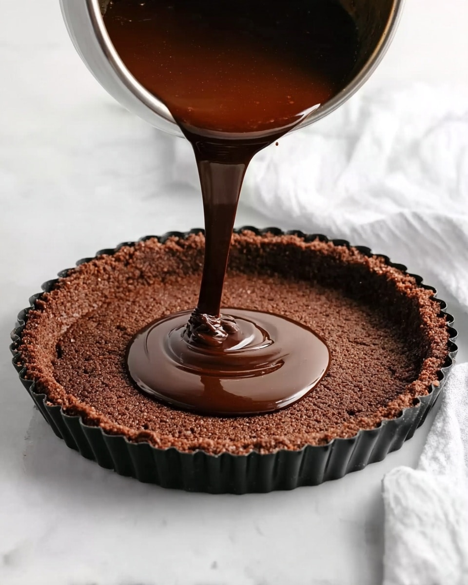 The image shows a dark brown chocolate filling being poured from a metal bowl into a round tart shell with rough, thick edges. The tart shell is dark brown and sits inside a black tart pan with scalloped sides. The chocolate filling is thick and smooth, creating a shiny pool in the center of the empty tart shell. The background surface is a white marbled texture, and a white cloth is partially visible on the right side. Photo taken with an iphone --ar 4:5 --v 7