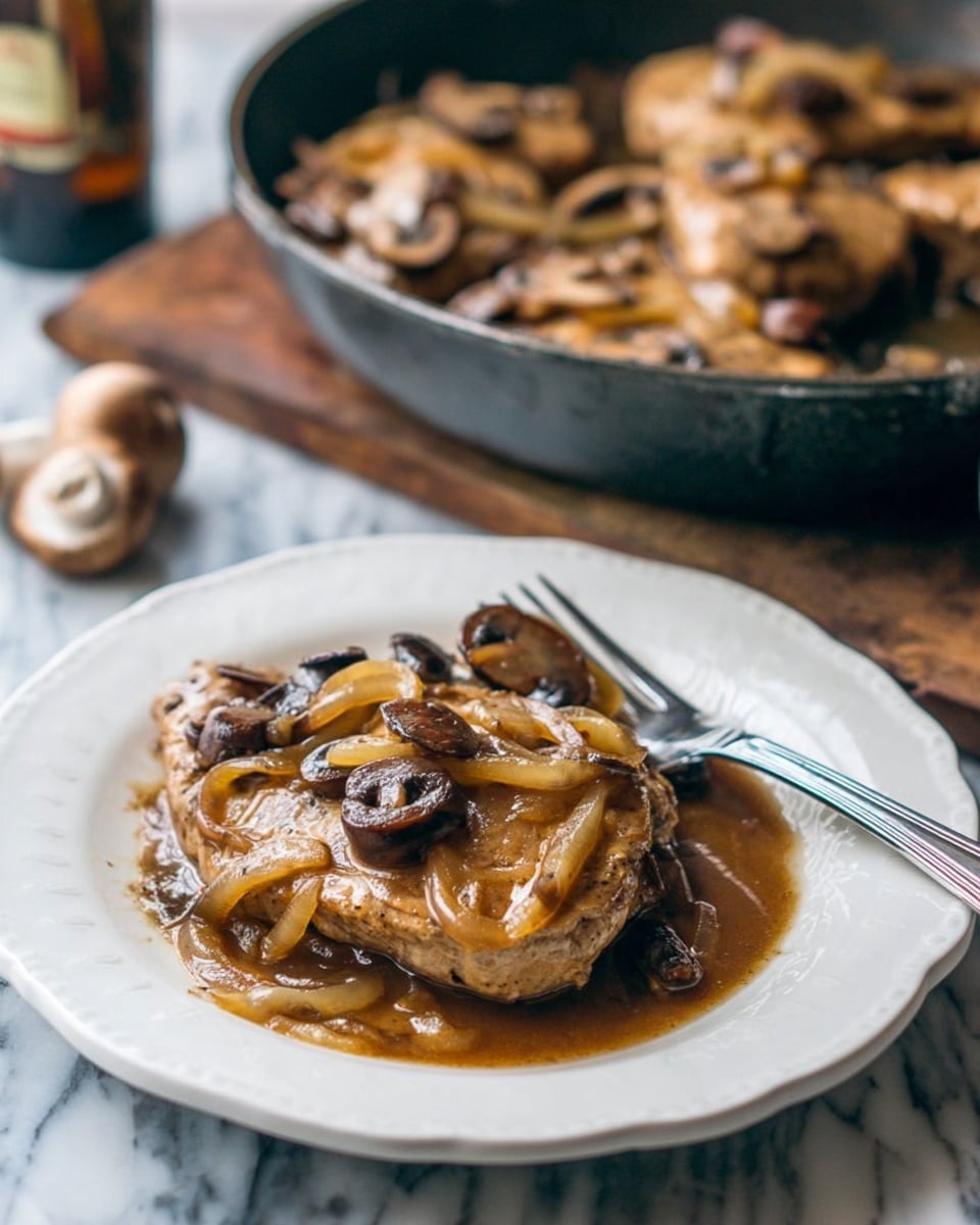 The image shows a white plate with one cooked piece of meat covered in brown sauce, topped with light brown cooked onions and darker brown mushrooms. The sauce pools around the meat, creating a shiny and slightly thick texture. A silver fork rests on the right edge of the plate. Behind the plate, there is a dark, round pan filled with more pieces of meat and the same onions and mushrooms, placed on a white marbled surface. Photo taken with an iphone --ar 4:5 --v 7