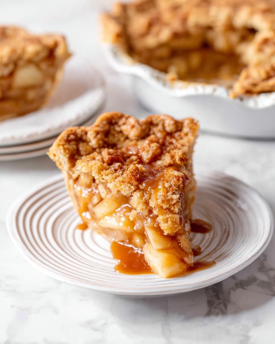 A single slice of crumb-topped apple pie sits on a white plate with spiral grooves, showing three clear layers: a golden brown crumbly top, a thick caramel drizzle above a juicy, translucent apple filling, and a light golden crust base. In the background, a pie dish with the rest of the pie is visible, with another slice on a white plate with a decorative edge. The setting has a white marbled surface that adds brightness and contrast to the warm colors of the pie and caramel. photo taken with an iphone --ar 4:5 --v 7